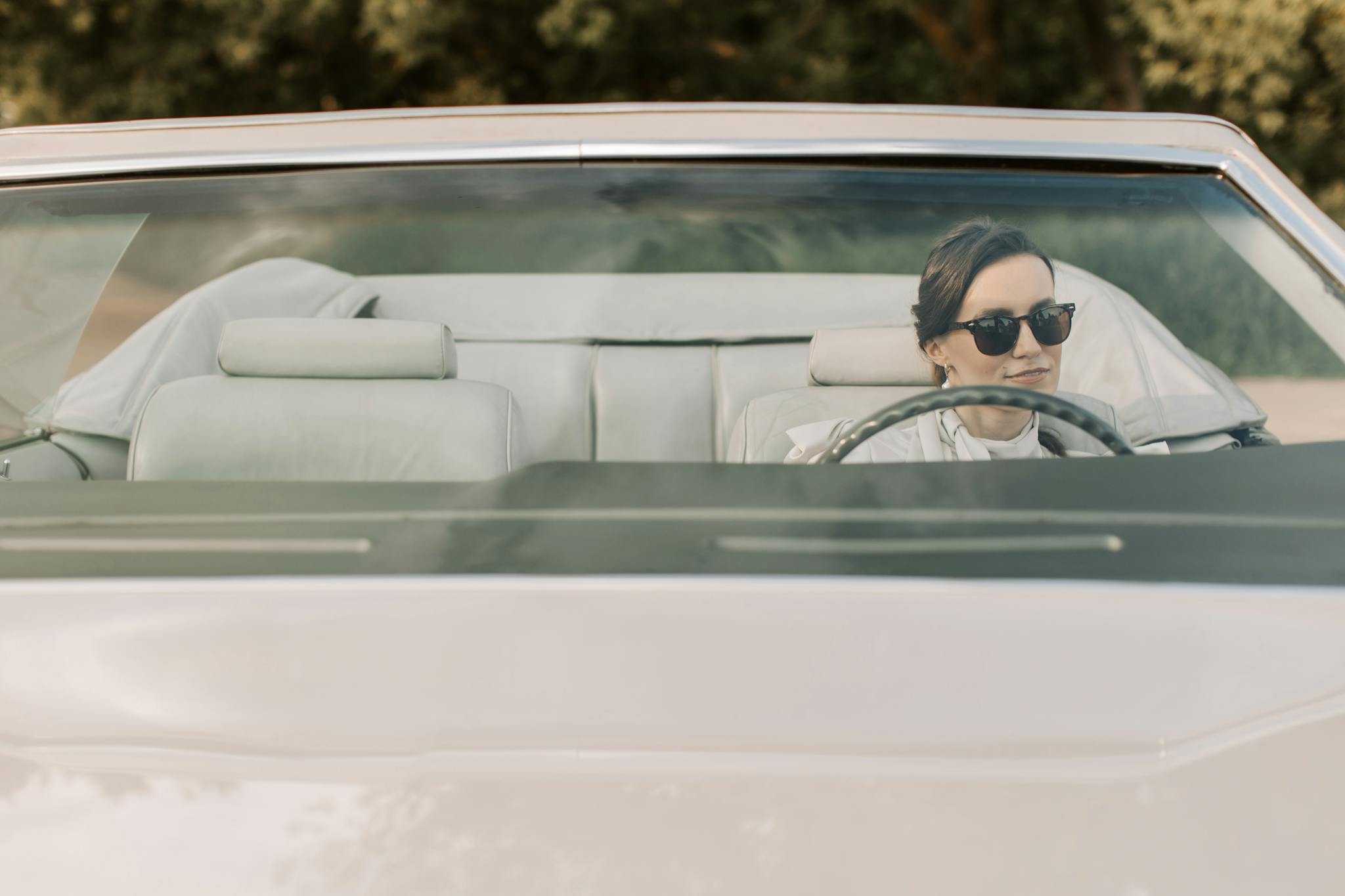 A woman in sunglasses driving a convertible car outdoors on a sunny day.