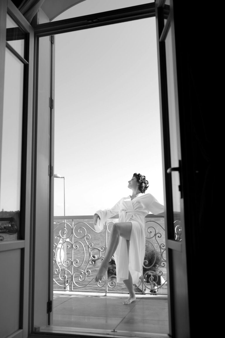 Black and white photo of a woman in a bathrobe relaxing on a balcony, enjoying leisure and elegance.
